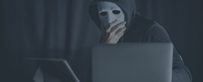 A person wearing white mask and dark hoodie using a computer.